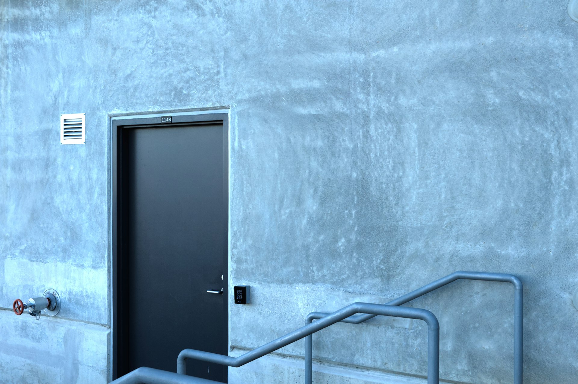 a door and a hand rail in front of a concrete wall