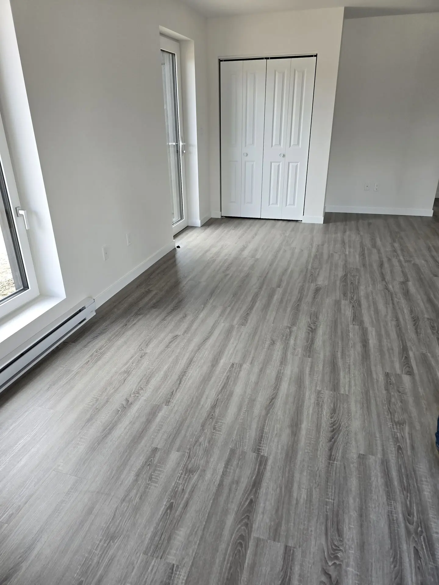 Cost-Effective SPC Flooring Sourced from China: Durable and Stylish Solutions Interior view of a room featuring gray SPC (Stone Plastic Composite) flooring, large windows, and closet doors.